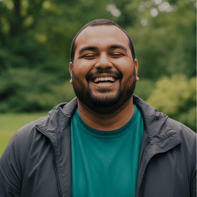 Man with a beard laughing outdoors in a teal shirt and grey jacket