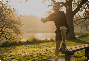 Man stretching against a bench in a park at sunrise